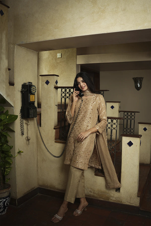 Woman in a beige traditional outfit standing in a room with decor elements.